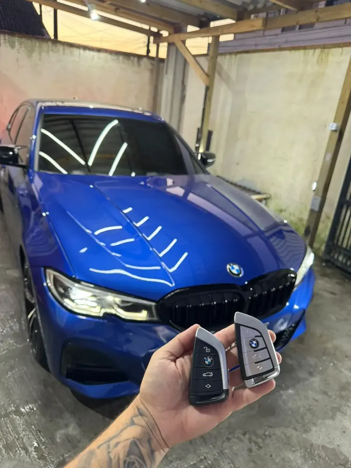 Duas chaves presenciais BMW em frente a uma BMW Série 3 azul