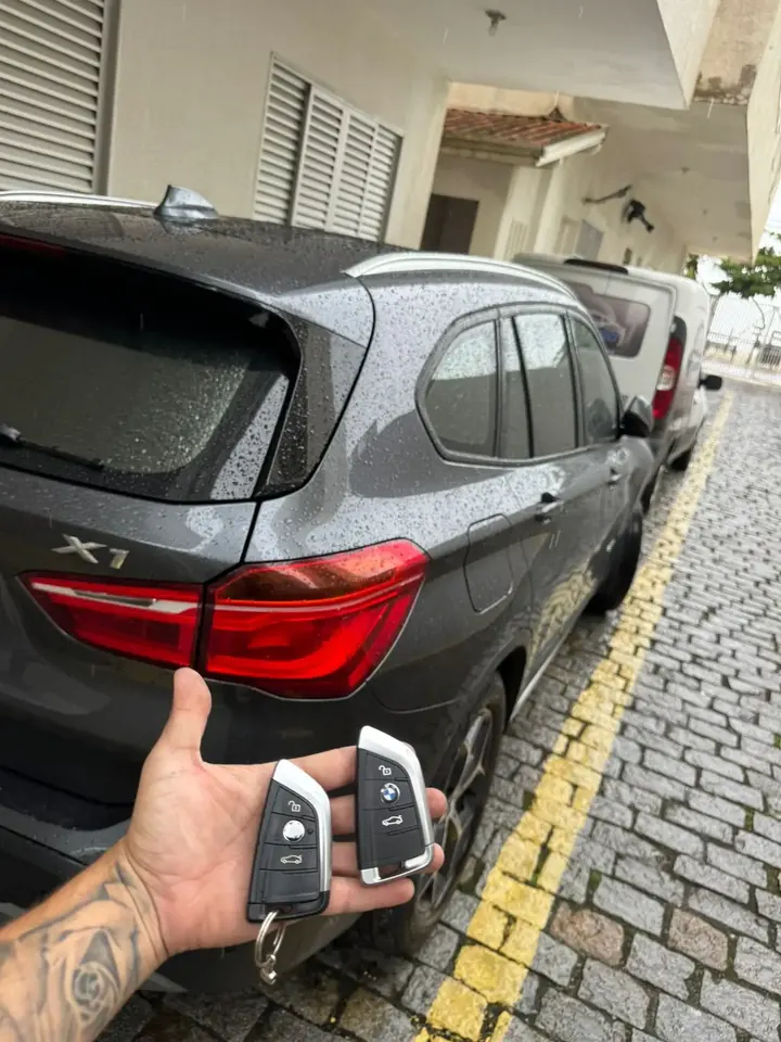Duas chaves BMW na mão do técnico ao lado de uma BMW X1 cinza