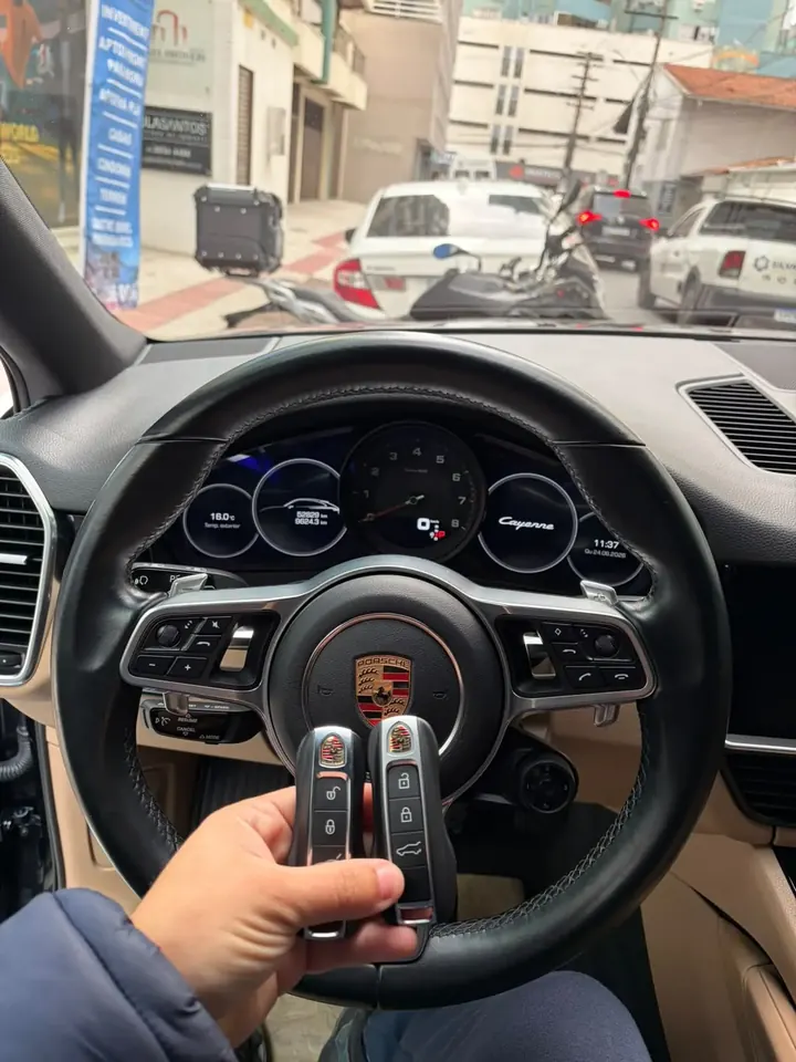 Par de chaves presenciais Porsche em frente ao volante de um Porsche Cayenne estacionado na rua em Balneário Camboriú