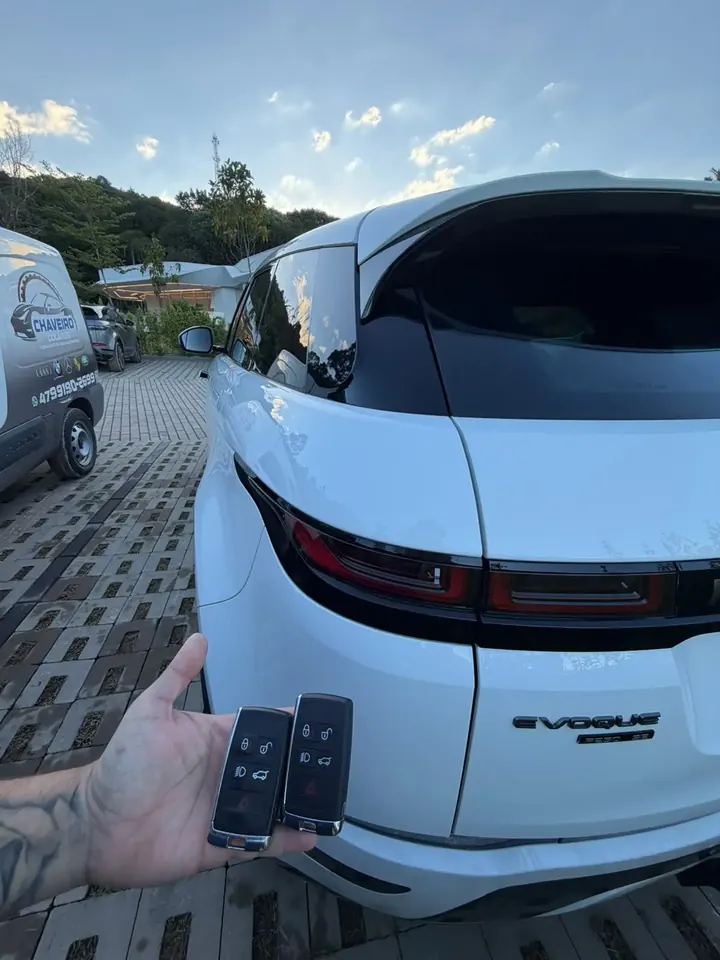 Técnico com duas chaves presenciais ao lado de um Range Rover Evoque branco, com a van do Chaveiro Colares ao fundo